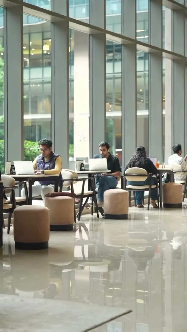 People working on laptops in the tall glass hall at Paper & Pie, RMZ Ecoworld