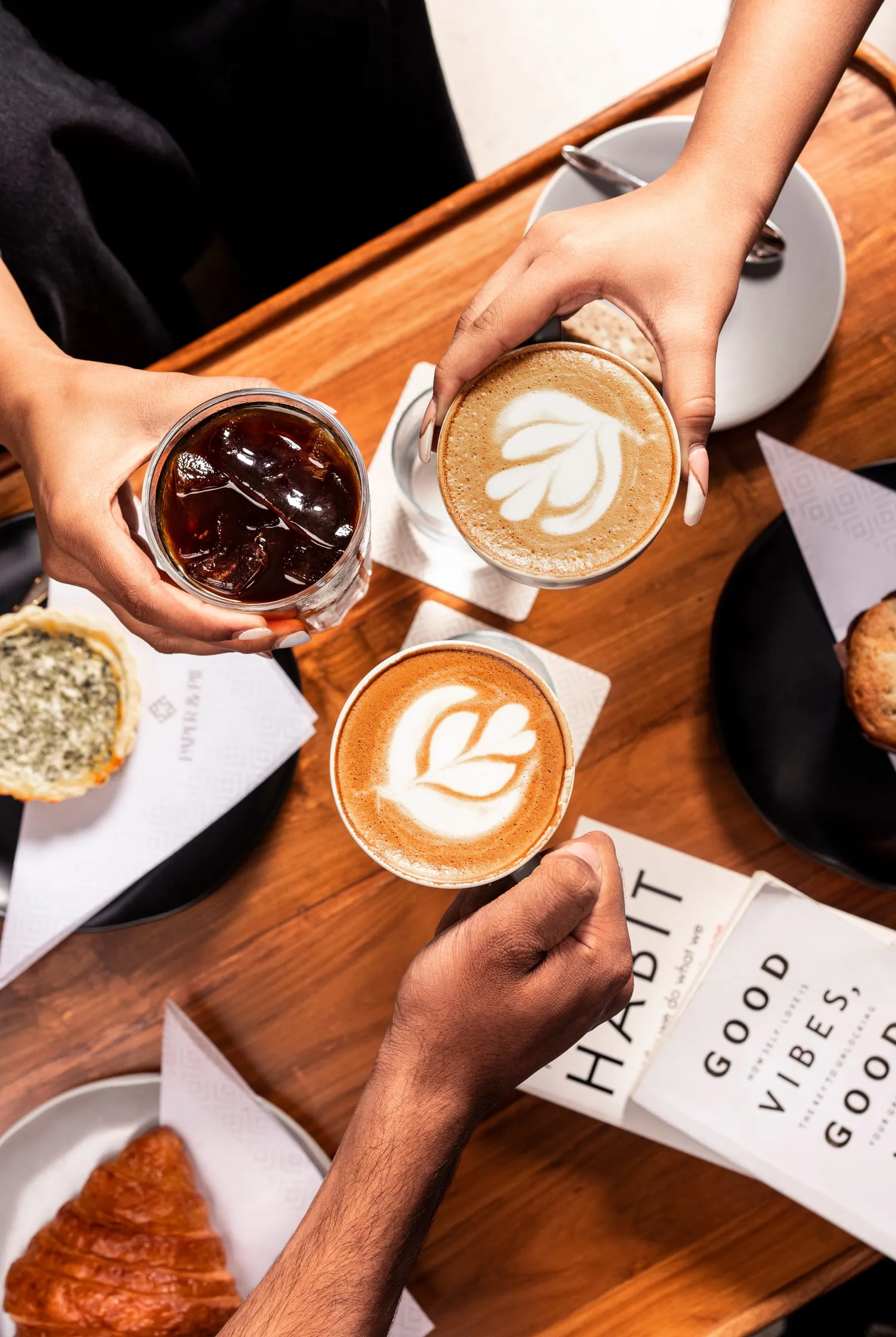 Friends sharing lattes and an iced coffee at a café table
